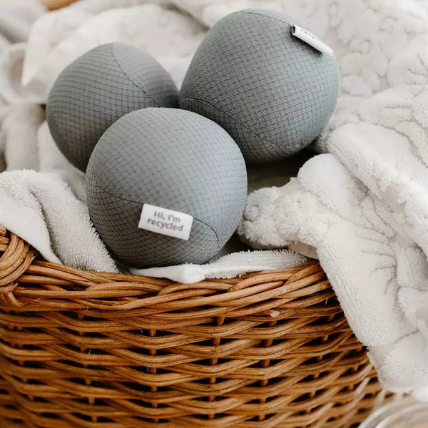 three antistatic vegan dryer balls made from recycled plastic water bottles. Color gray, sitting on top of white towels in a basket. three antistatic vegan dryer balls made from recycled plastic water bottles. Color gray, sitting on top of white towels in a basket.
