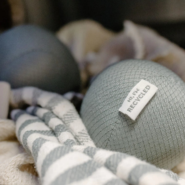 three antistatic vegan dryer balls made from recycled plastic water bottles. Color gray, sitting on top of white towels in a basket. three antistatic vegan dryer balls made from recycled plastic water bottles. Color gray, sitting on top of white towels in a basket.