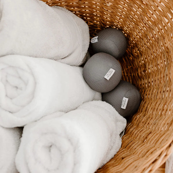 three antistatic vegan dryer balls made from recycled plastic water bottles. Color gray, sitting on top of white towels in a basket. three antistatic vegan dryer balls made from recycled plastic water bottles. Color gray, sitting on top of white towels in a basket.