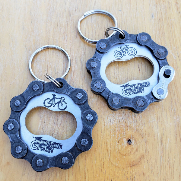 Two bicycle chain bottle openers on a wooden surface with key rings attached