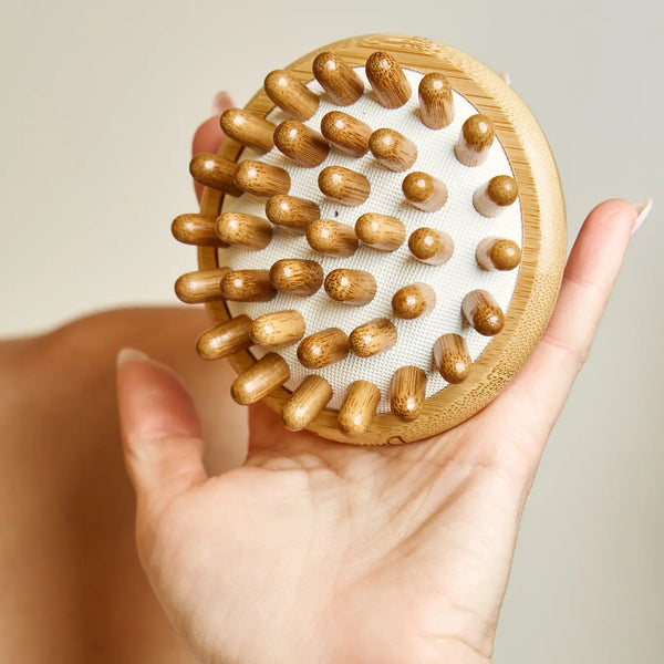 Hand holding a wooden scalp massage tool with raised knobs on a neutral background