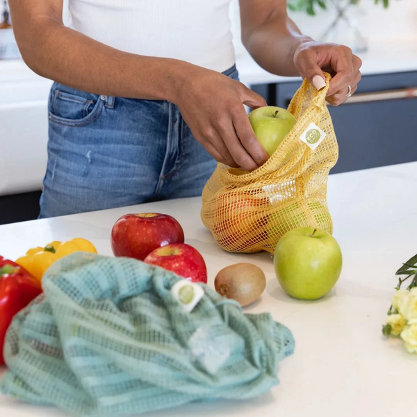 Person using a yellow mesh produce bag with fruits on a kitchen counter.