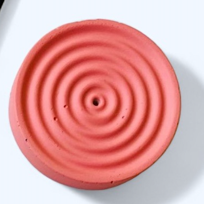 Pink circular incense holder with concentric rings on a white background
