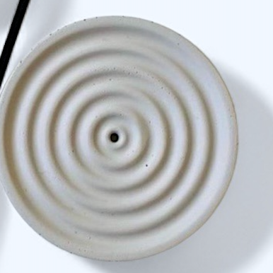 Close-up of gray incense holder with concentric circular patterns on a white background