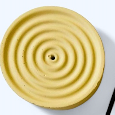 Round yellow ceramic incense holder with concentric circular patterns on a white background