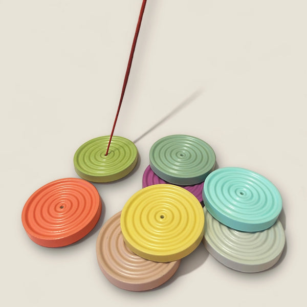 Colorful circular incense holders with a single red incense stick on a beige background