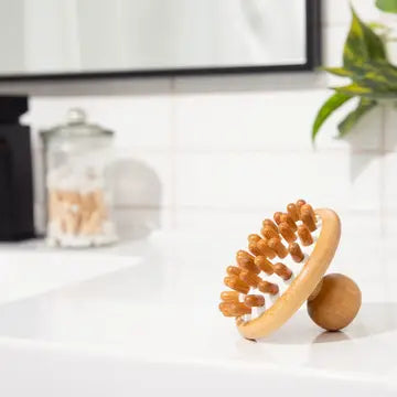 Wooden massage tool on a white surface with a mirror and plant in the background