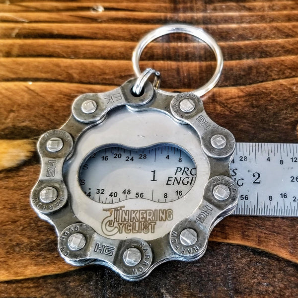 Metal key chain bottle opener held up against a ruler to show bottle opener hole is approx. 1.5" wide