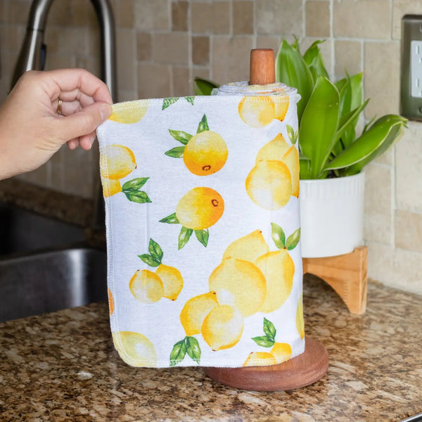 Hand holding a reusable paper towel with lemon pattern on a kitchen counter.