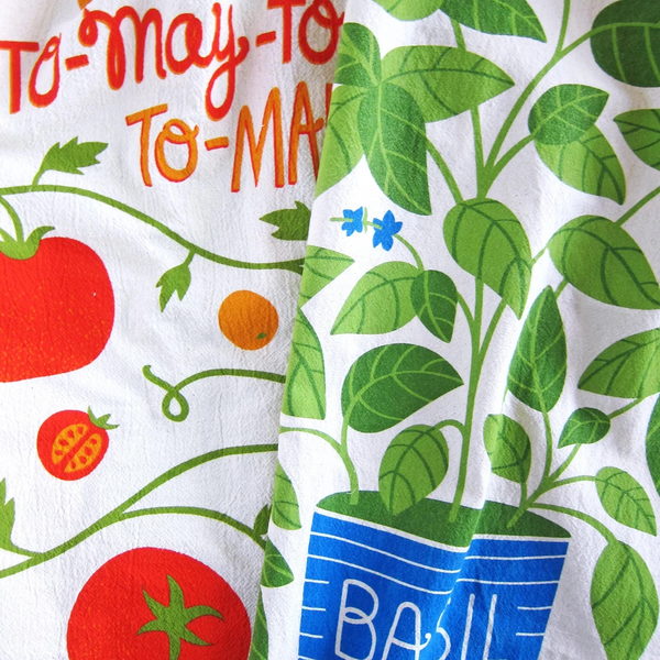 Two dish towels with tomato and basil designs on a white background