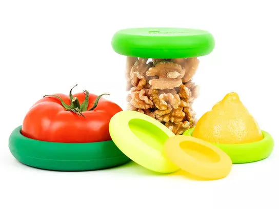 Picture of five different sized silicone food huggers that act as covers for food. One shown covering the cut side of a tomato, one over the half of a lemon and one as the lid of a jar
