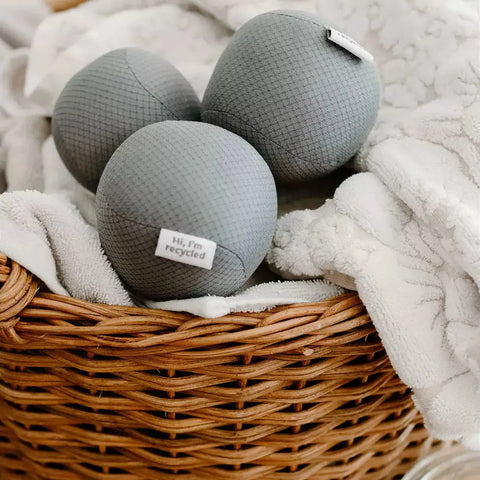 three antistatic vegan dryer balls made from recycled plastic water bottles. Color gray, sitting on top of white towels in a basket.